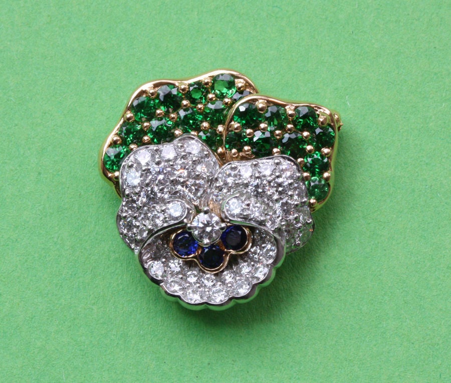 A brooch in the shape of a pansy set with 23 brilliant cut tsavorite garnets (circa 1.1 carats) in 18 carat gold and 51 brilliant cut diamonds (circa 2.1 carats) set in platinum, the heart of the pansy is set with 3 brilliant cut sapphires, signed