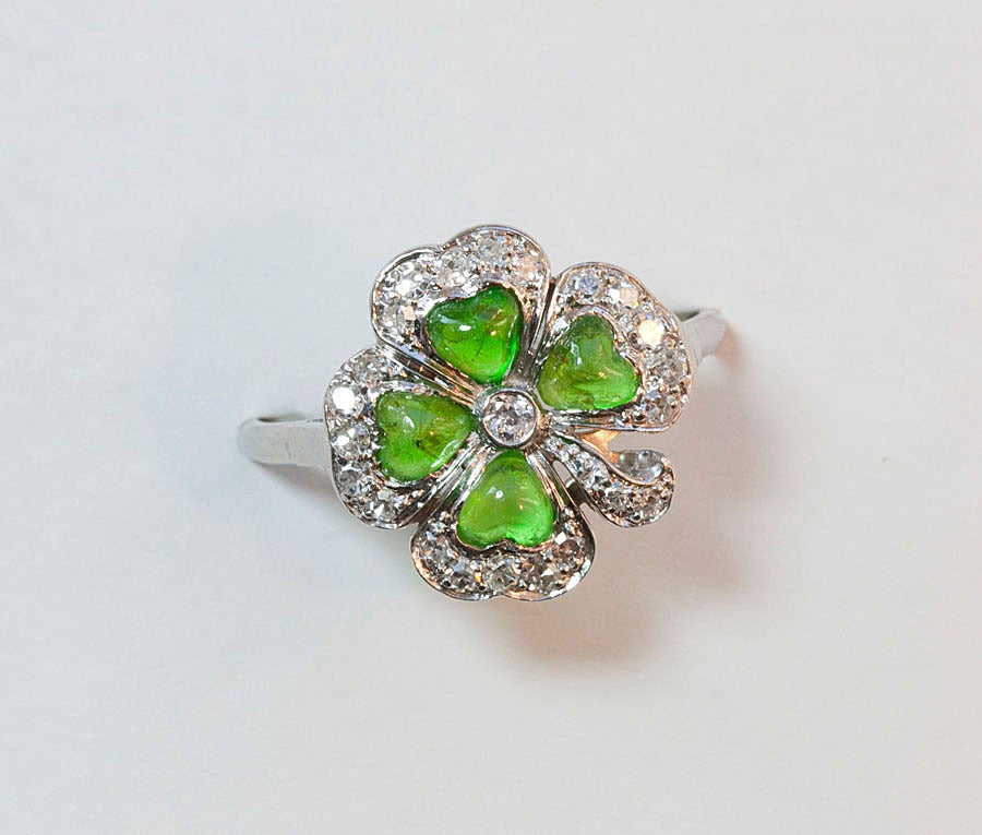 A delicate platinum ring in the shape of a clover set with single cut diamonds and 4 heart shaped cabochon demantoid garnets in the centre of each clover leaf, V.S., circa 1915.

weight: 3.1 grams
ring size: 16.75 mm. 5 1/2 US.