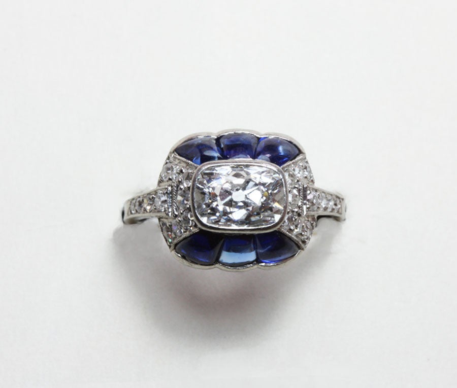 A platinum Art Déco ring with a cushion shaped diamond in its centre (colour G-H almost 1 carat) surrounded by brilliant cut diamonds on the sides and shoulders and six suiffé cut sapphires, signed and numbered: Linzeler & Marchak, 1421, Paris,