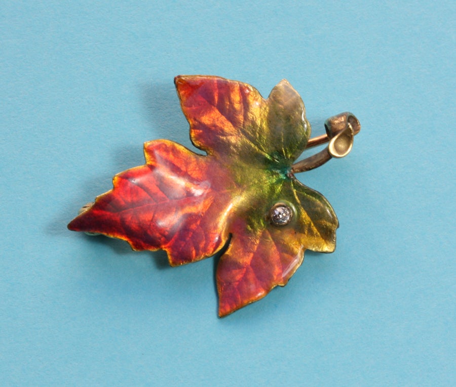 A small 14 carat gold brooch in the shape of a mable leaf with beautiful fall colored red, pink, yellow, gold and green enamel and a small brilliant cut diamond, signed: Krementz & Co., U.S.A., circa 1900.