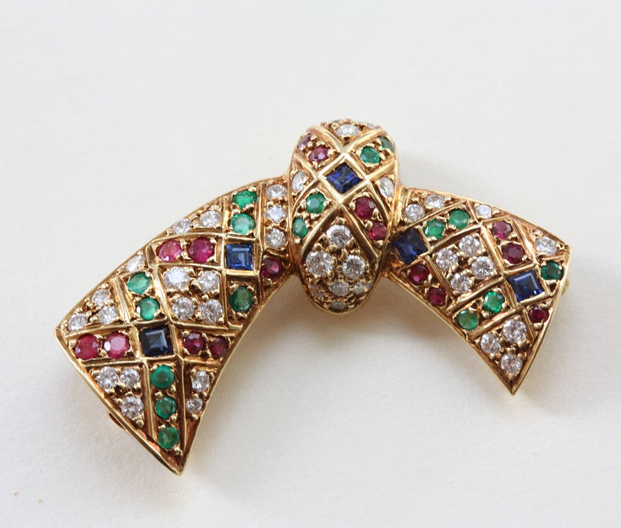 A cute 18 carat gold bow brooch set with small brilliant cut diamonds, rubies and emeralds and square cut sapphires in a plaid motive, signed and numbered: Van Cleef & Arpels, 1980s.