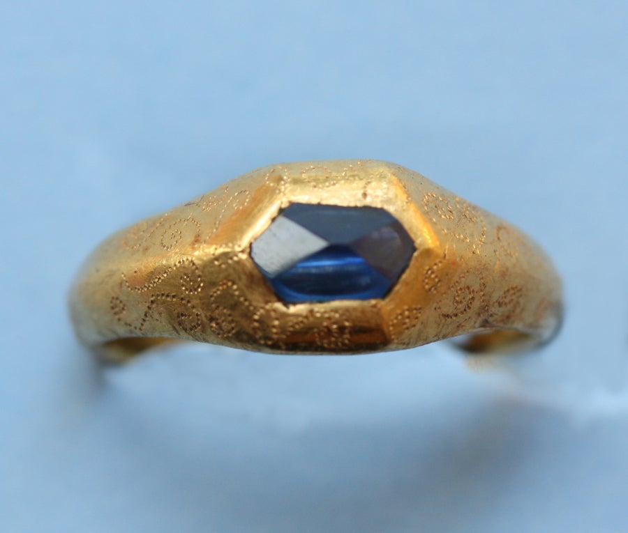An important high carat gold medieval ring set with a natural irregular octahedron cut sapphire, decorated with fine engravings and inscribed on the inside of the shank with the text 'Loyal Desir' which means legal or loyal desire which indicates
