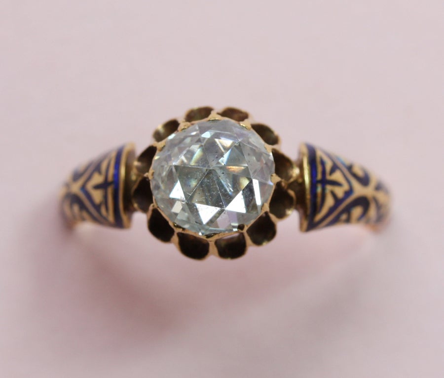An 18 carat gold ring set with a large crown rose cut diamond (app. 1 carat), in the shank are blue enamel floral decorations, master mark, French, 19th century.

weight:
ring size:
