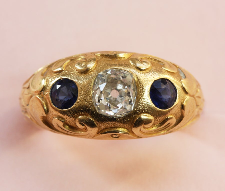 A very pretty three stone ring; 18 carat gold beautifully engraved set with two synthetic sapphires (app. 0,3 carats) and a cushion cut diamond (app. 0.75 carats), master mark MS around a beehive, France, circa 1935.

weight: 11.1 grams
ring