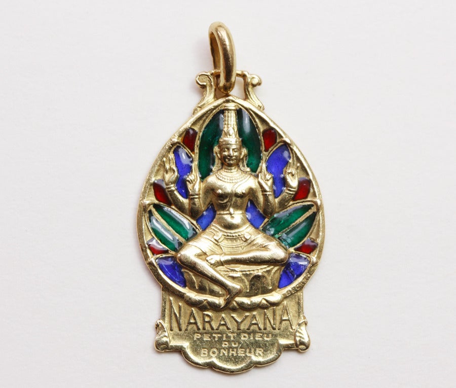 A lucky pendant with multi colored plique-a-jour enamel representing Narayana or Vishnu, the supreme god with four arms in Hindu mythology. Here Vishnu is called ‘le petit dieu du bonheur’ signed: Becker for Edmond-Henri Becker, the French engraver