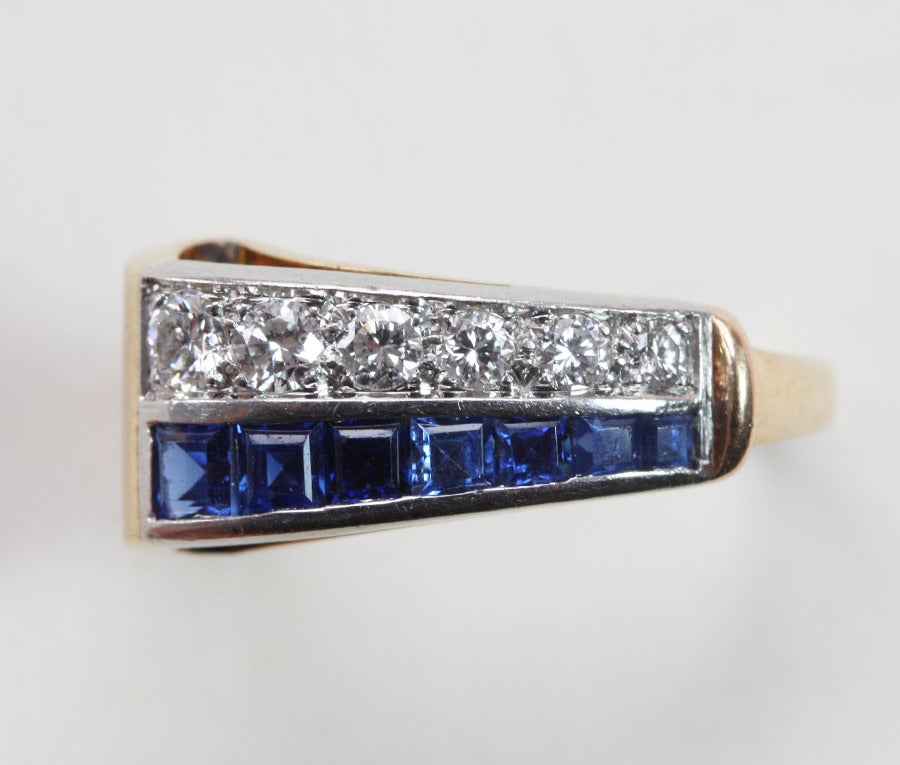 A 14 carat gold swirl ring set with a line of brilliant cut diamonds and one with square cut sapphires both set in platinum, USA, signed: C.J. Auger, circa 1935.

weight: 4.5 grams
dimensions: 15.25 mm. 4 ½ US