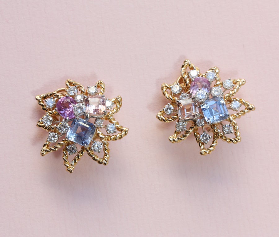 A pair of 18 carat gold flower ear clips set with 13 brilliant cut diamonds (total circa 2.2 carat), an oval cut pink sapphire (total circa 1.5 carat), a square cut light blue sapphire (total circa 2 carat) and a peach colored sapphire (total circa