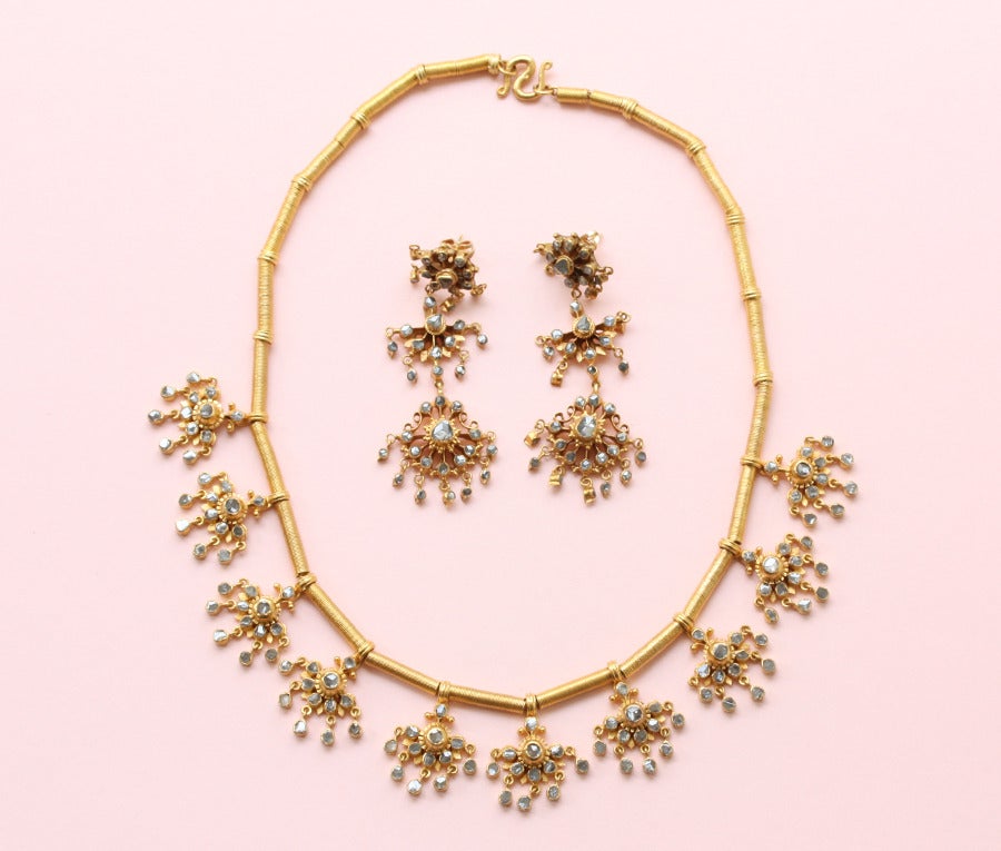 A 20 carat gold demi suite consisting of earrings and a necklace of gold beads on a chain with ten flower shaped elements with little drops all set with small rose cut diamonds, as are the earrings, India.

weight: 59.4 grams
length: earrings: