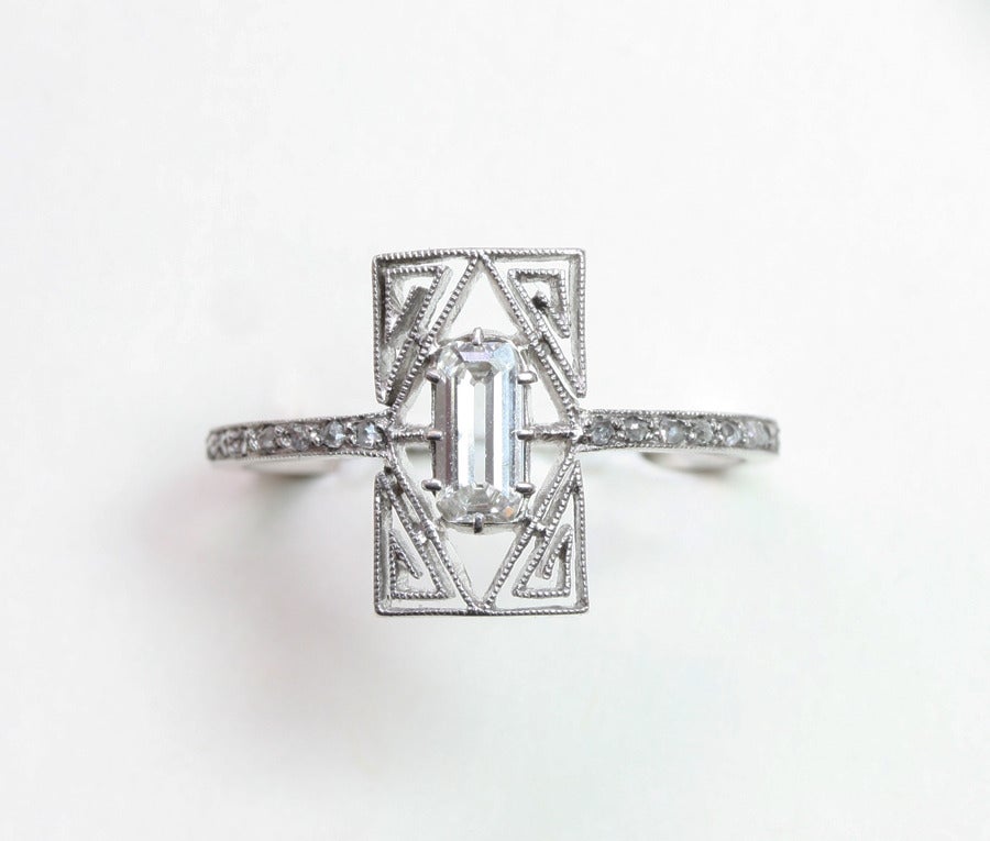 An elegant platinum ring set with a bauguette cut diamond and with in the four corners a meander shaped platinum decoration in mille griffe, the shank is decorated with small rose cut diamonds, French platinum mark, signed: LALIQUE, France, circa
