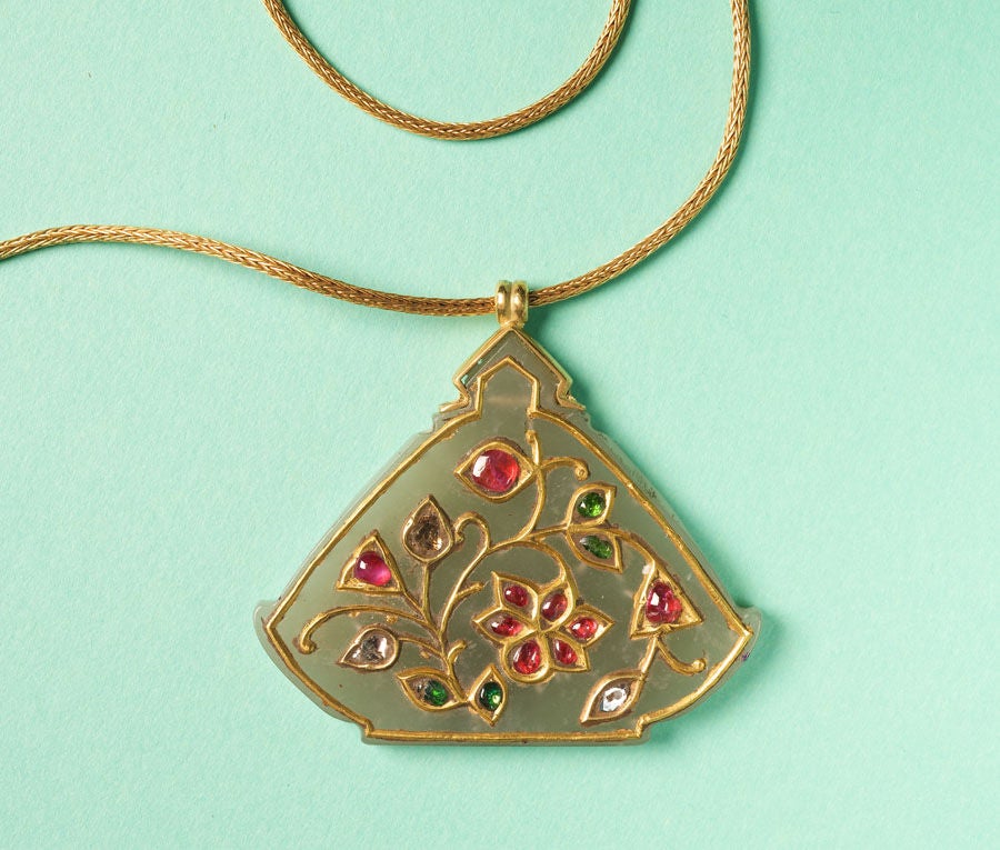 A Haldili amulet; a jade tablet Encrusted with pure gold, rubies, emeralds and diamonds with floral motives, around 1800, India, hanging from a high carat gold woven chain.

This Islamic amulet symbolises the illumination of the heart by
