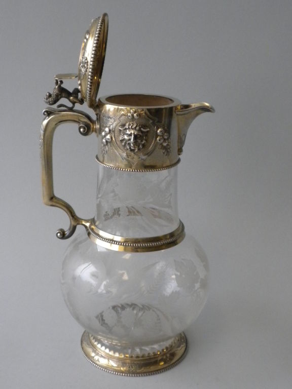 This is a fine English Sterling Silver Gilt Mounted Crystal Decanter made by John Figg, London, 1860.  The spherical crystal body with a cylindrical neck, is mounted in gilded sterling with cast and chased satyr maskhead motifs.  The hinged lid is