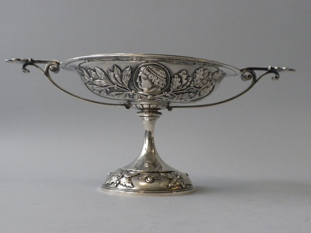 This beautifully crafted mid-nineteenth century Greco-Roman styled Sterling Silver Compote is decorated with applied neo-classical heads and acanthus and laurel leaf wreaths.  The rim is decorated with an applied Greek key border and anthemion