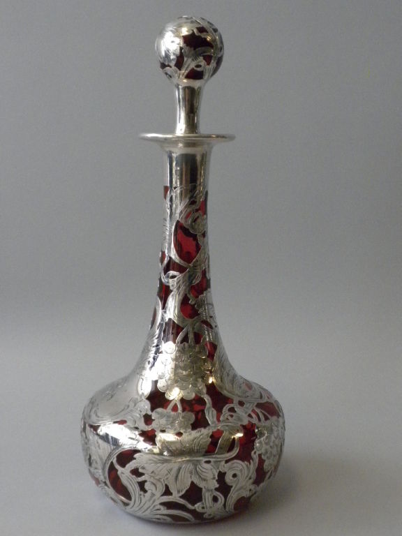 This Gorgeous Decanter, Circa 1900, is a prime example of American Sterling Silver Overlay and Cranberry Glass at its best. Although unmarked, this decanter is made of the highest quality craftsmanship. The cranberry glass is overlaid with silver in