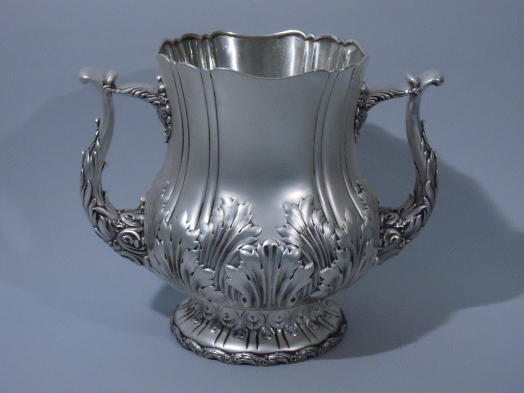 Two-handled sterling silver trophy cup. Made by Whiting, C 1890. Baluster body with 2 bracket handles on dome foot. Incised lines, foliage, and stylized egg-and-dart motif. Scalloped rim and foot rim, the latter encircled with flowers and foliage. A