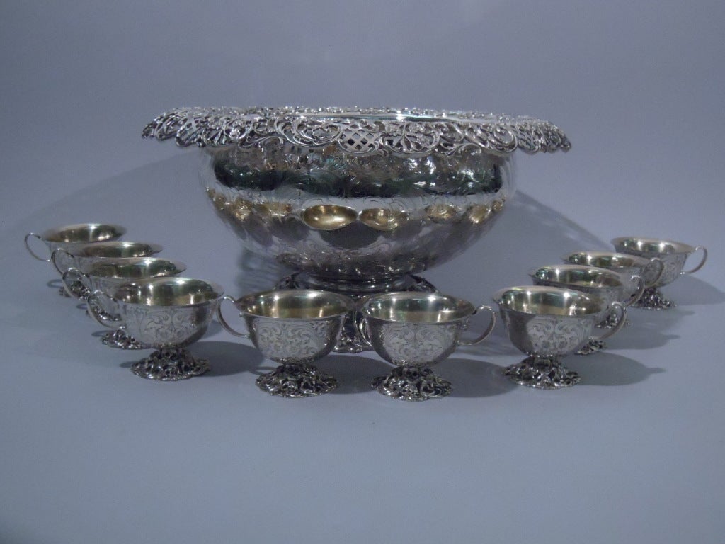 Sterling silver punchbowl and 10 cups. Made by JE Caldwell in Philadelphia, ca. 1890. Punch bowl: Curved sides, rolled rim, and dome foot. Cups: curved bowl, flared rim, scroll handle, and dome foot. Interior is gilt. All: Feet and rim have open