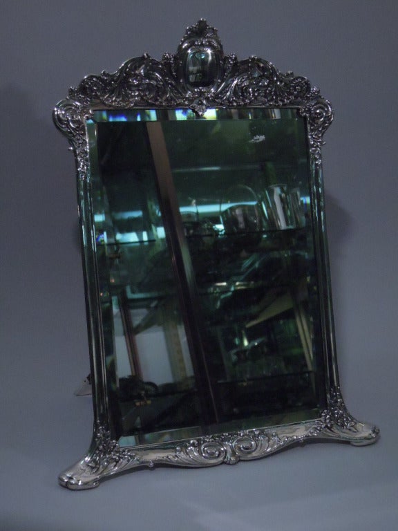 Sterling silver vanity mirror. Made by Tiffany in New York, ca. 1900. Rectangular silver frame with straight molded sides, curvilinear bottom with 2 scrolled feet, and repousse crown: central oval cartouche between 2 lionâ??s heads set in foliate