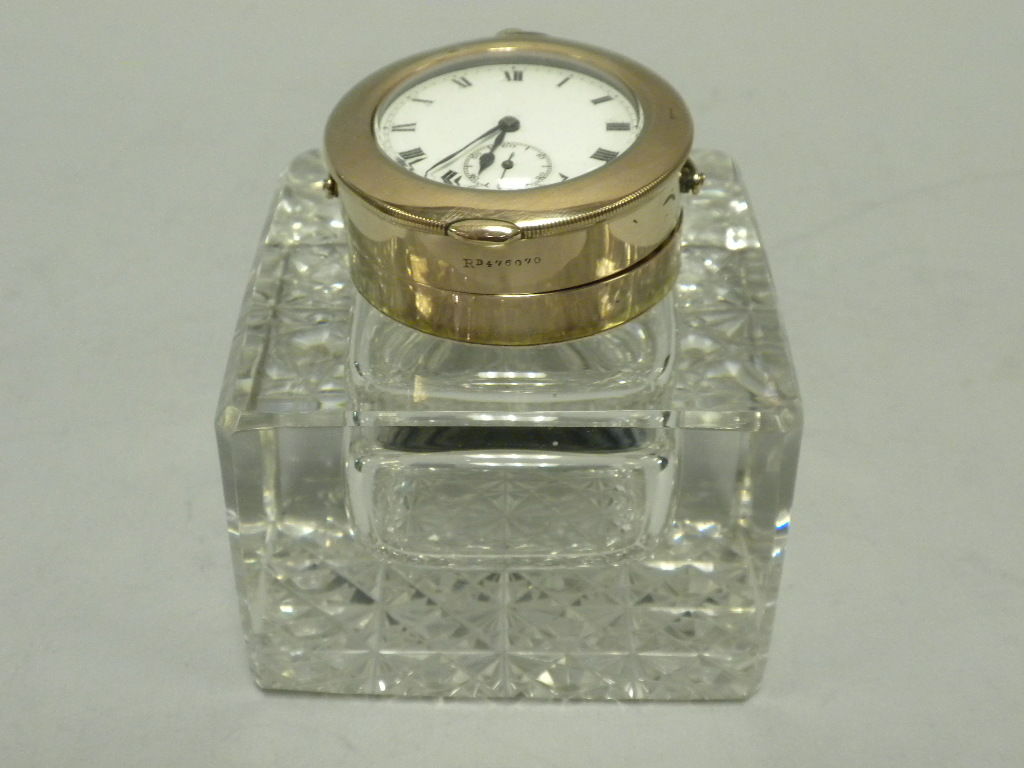 This Inkwell is a lovely example of Edwardian Novelty Items.  It is designed as a square crystal inkwell with starburst cut base and plain body.  The lid is designed as a 9 carat gold encasement for an open-faced watch.  The lid is hallmarked with