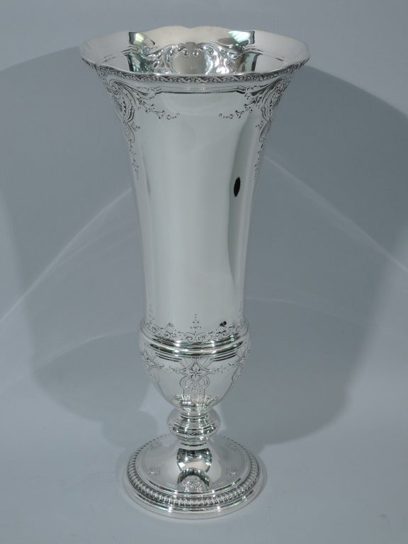 Large sterling silver trumpet vase. Made by Tiffany in New York, ca. 1917. Sides taper to baluster bottom on knopped support on raised foot. Repousse foliage, flowers, and strapwork. Scalloped rim bordered with raised floral guilloche. Foot rim is