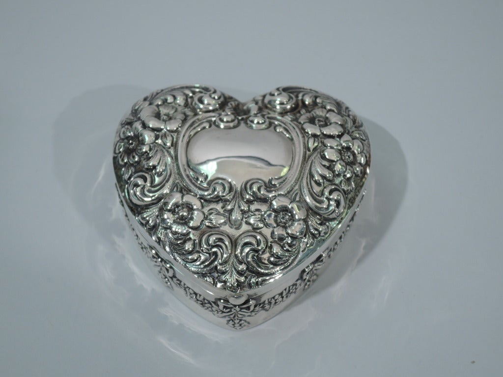 Sterling silver heart-form jewelry box. Made by Mauser in New York, ca. 1900. Box sides bordered by floral garlands with ribbon bows and pendant flowers. Cover is hinged with repousse flowers and scrolls and central scrolled cartouche (blank for