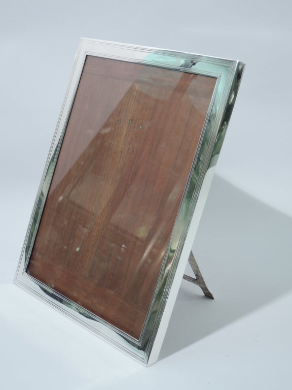 Sterling silver picture frame. Rectangular with incised linear borders. Made by Tiffany in New York, ca. 1910. With glass, stained-wood back, and hinged support for vertical display. The pattern (no. 16545D) was first produced in 1905.