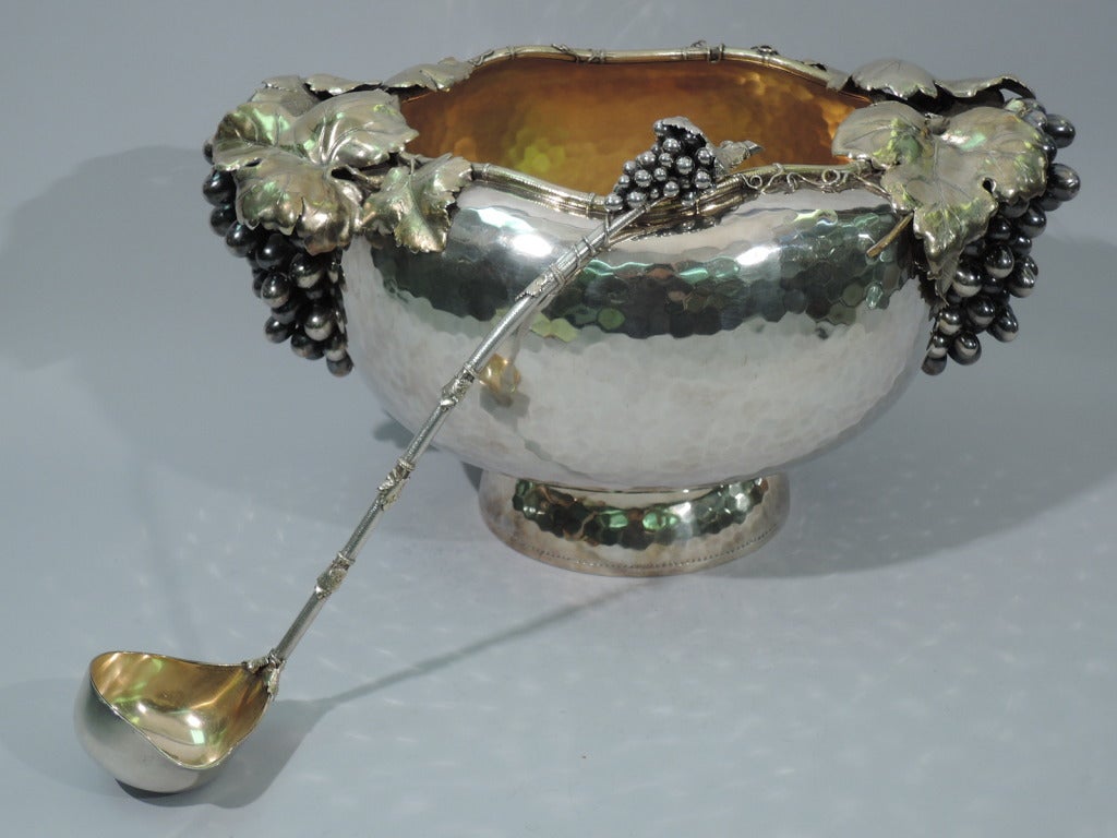 Sterling silver punchbowl with grape bunches. Made by Gorham in 1881. Bowl has curved sides and rests on dome foot. Hammered honeycomb exterior and gilt interior. Grape bunches and leaves applied to two sides. Mouth has scalloped rim encircled with