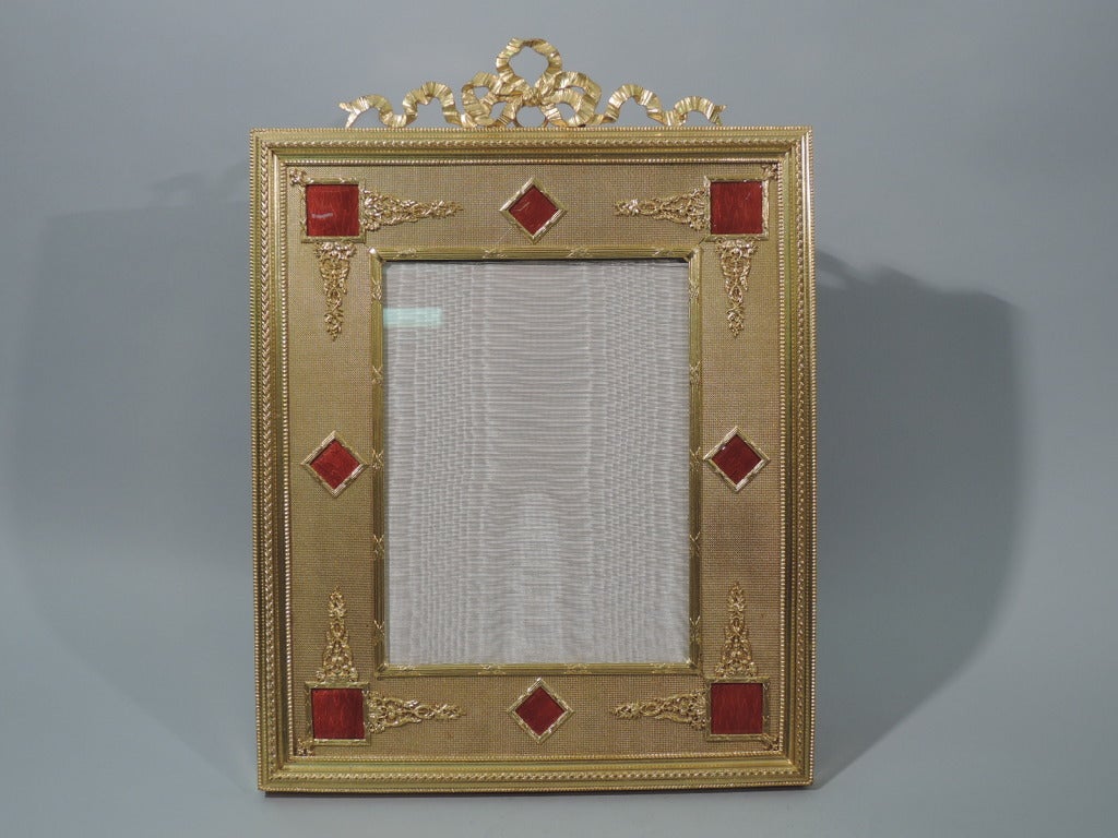 Large dore bronze frame with red enamel. Made in France, ca. 1900. Reeded and rectangular window bordered by rectilinear plaques in red enamel (some with applied foliage) on stippled ground. Rim has beading, and foliate and conical ornament. Ribbon