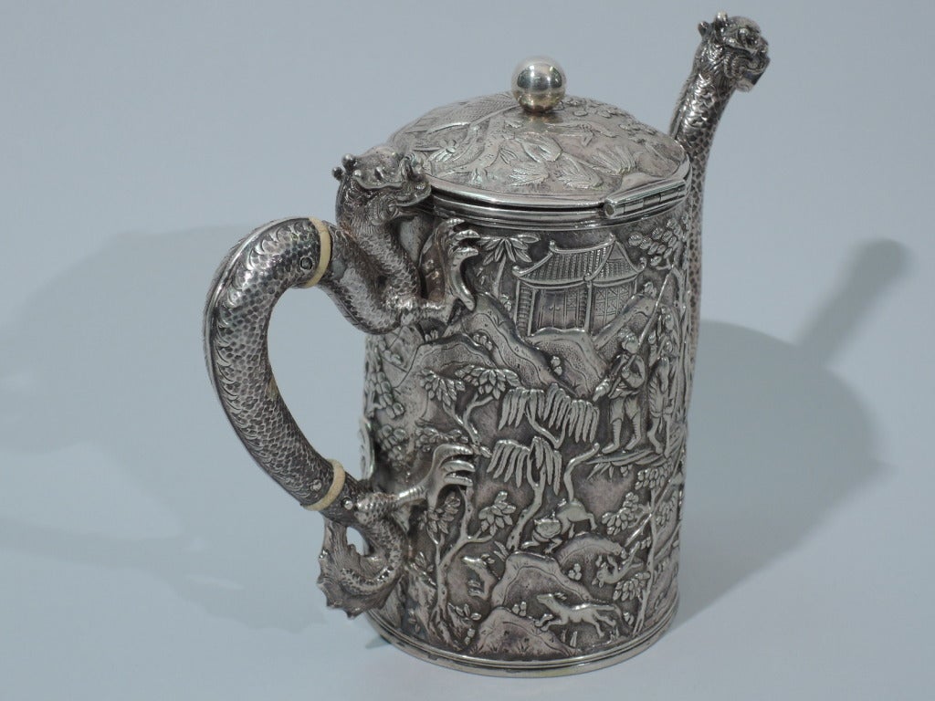 Dramatic silver teapot. Made by Khecheong in Canton, ca. 1850. Upward tapering sides, side-hinged and curved cover, scroll handle, and scrolled vertical spout. The sides have raised scenes of Chinese life with figures in exotic costumes, pavilions,
