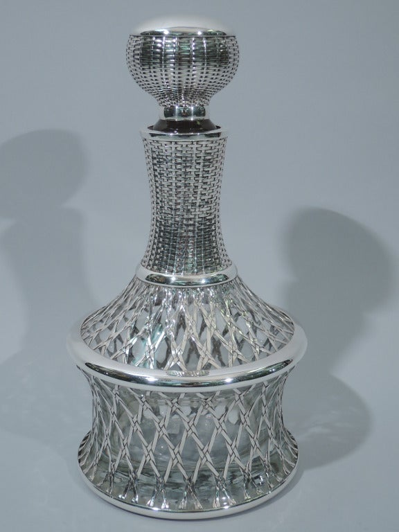 Japanese clear glass decanter and stopper with 970 silver basket overlay, ca. 1920. The decanter is concave with concave cylindrical neck. Ball stopper has short plug. Basket-weave overlay. Stopper top is solid silver. Hallmarked “Silver 970.”