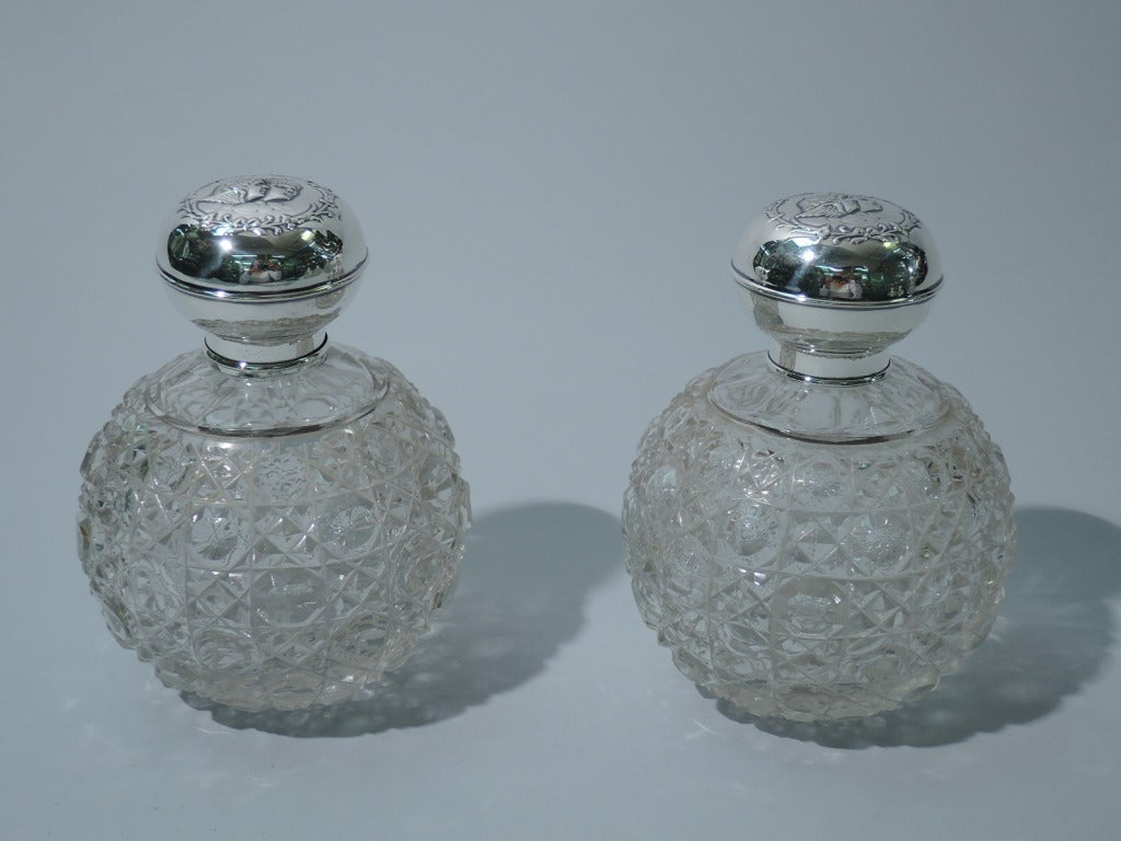 Pair of Edwardian perfume bottles in cut clear glass and sterling silver. Made by Henry Matthews in Birmingham in 1907. Bottles: globular with cut ornament and short neck in silver collar. Stopper is faceted with short and tapering plug. Covers: