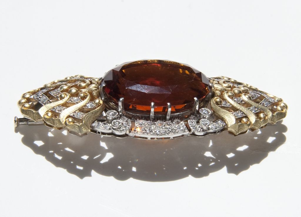 This stunning brooch bridges the designs of art deco and the emerging cocktail jewelry of the retro period with a pavé of diamonds, baguette cut diamonds, and a natural Madeira citrine measuring approximately 26.76mm x 21.44mm x 12.76mm.  
The gold