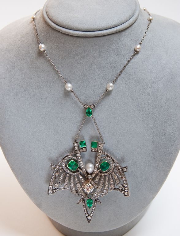 This stunning Art Nouveau pendant necklace features a 1.40 carat mine cut diamond surrounded by two cushion cut emeralds, two pear shaped emeralds and two square step cut emeralds, totalling approximately 4.64 carats. The pendant is set with 243 old