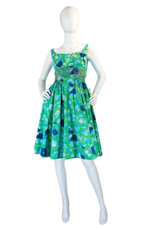 This is a gorgeous Malcolm Starr with a spectacular print in bright blues and greens on a crisp cotton backdrop. A simple cut, sleeveless bodice has a scooped neck and a V shaped back. The waist nips in and has a spectacular band of clear beads and