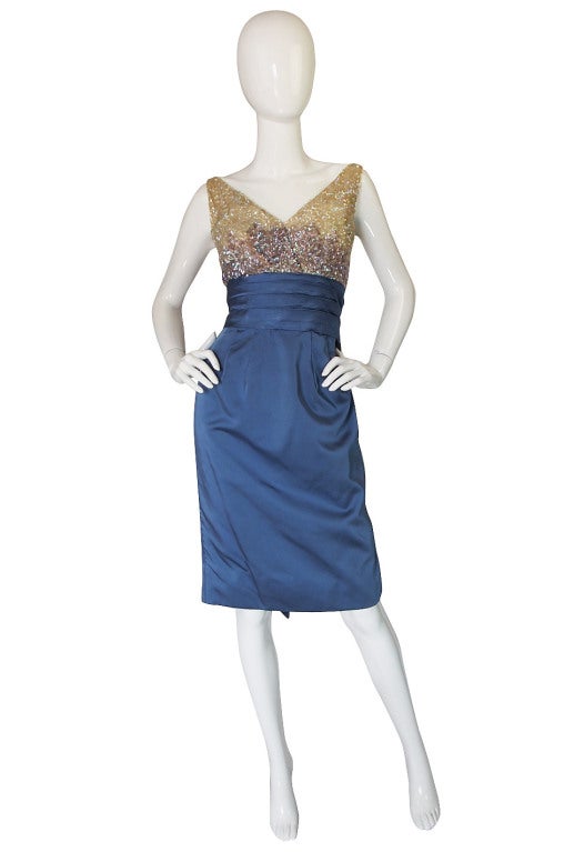 The top portion of this lovely dress features iridescent sequins that are hand applied and gradually change from cream to blue as they near the waistline. The halter top crosses at the front and dips to the waist at the back. Silk cinches in the