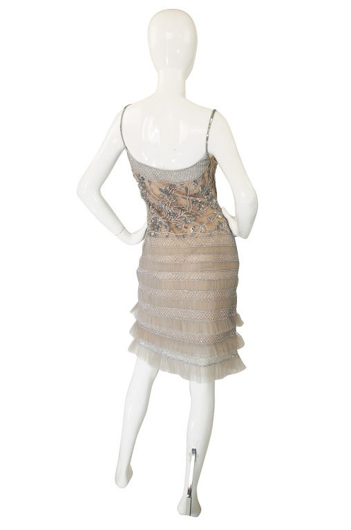 This couture quality constructed cocktail dress that it is elaborately beaded and sequined by hand. The color is a pale silver grey and a fine silk net is set over an interior nude lining. This has then been shaped around the hips by gathered