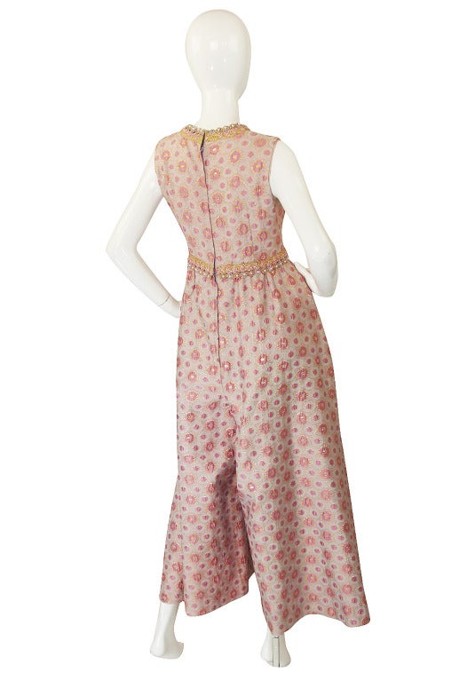 This is a fantastic 1960s jumpsuit in a light pink brocade , upon which gold thread has been worked in so that the entire piece glows when you move. The pattern is fantastic - part of the pink is a deeper tone and slightly puffed to it has a pretty,