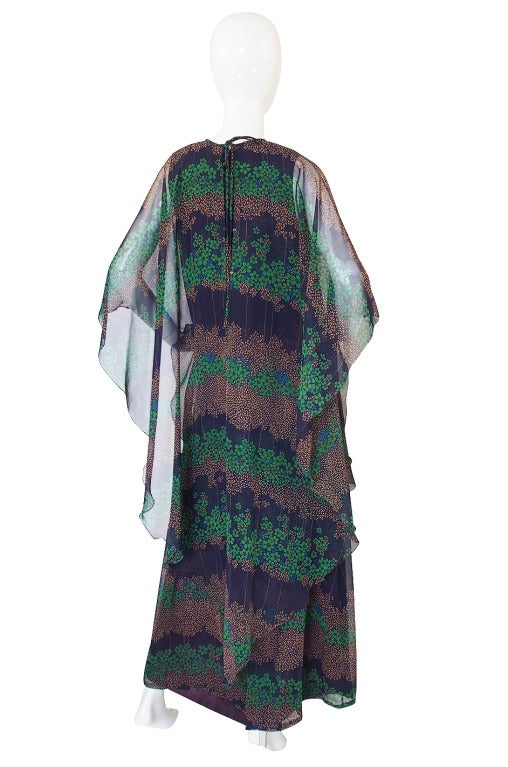 This late 1960s, early 1970s chiffon caftan dress by Jean Varon has layers of beautifully printed chiffon that cascades down to the ground. Everything about this piece is pretty and romantic. An attached top cape like layer flows over the interior
