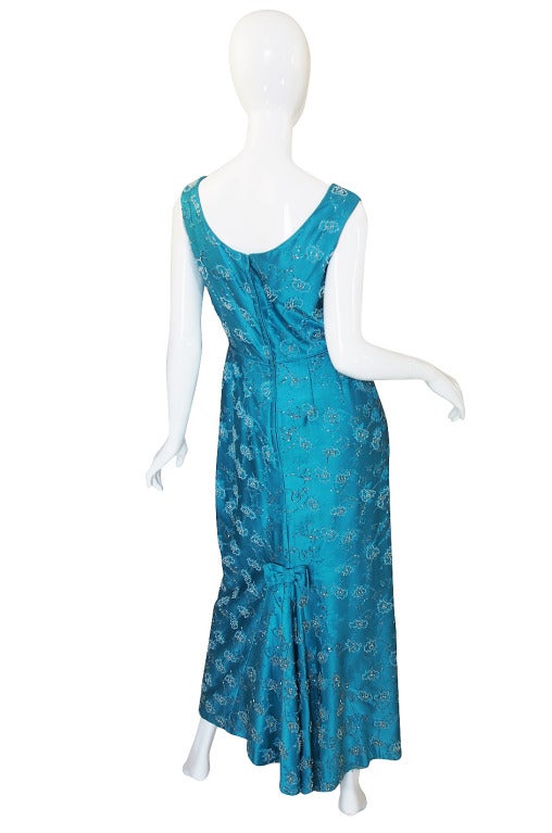 I always have a soft spot for these formal beaded 1950s gowns and it is very unusual to find one in such a magnificent color! The satin base is a deep azure turquoise blue and it is quite beautiful. The fabric has a floral pattern worked through it