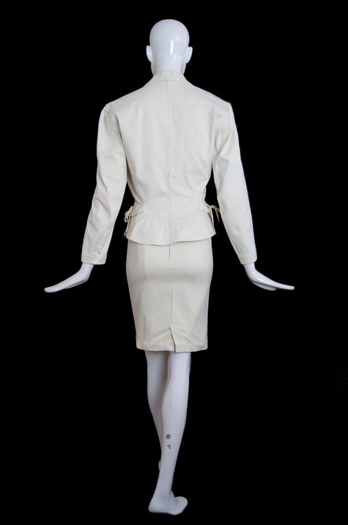 A fantastic, sexy curve enhancing suit from Azzedine Alaia in an almost canvas like cotton fabric. The thickness of the fabric allows the jacket to hold shape and give it extra structure. It's nipped in at the waist and the waist-line further