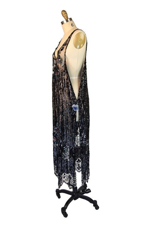 Exquisite 1920s piece has some of the most phenomenal sequin work I have yet to see. The base of the dress is a black fine silk netting. Onto this has been hand applied row after row of glossy black sequins with an amazing floral design worked in