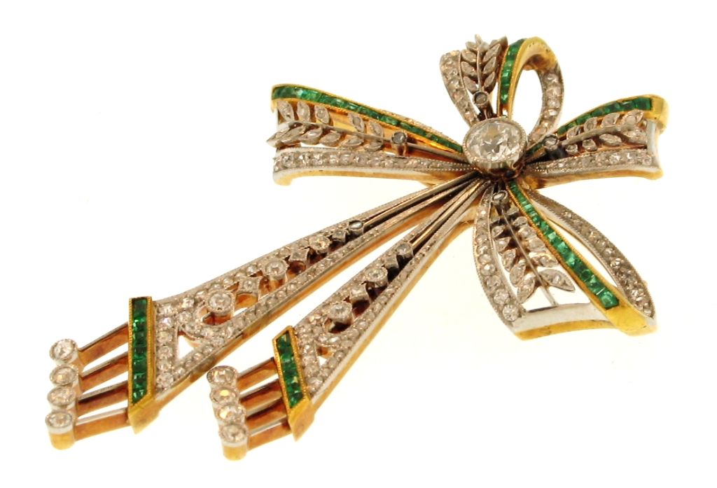 18k yellow gold and platinum Edwardian emerald and diamond ribbon and bow pin with one old mine cut diamond weighing 0.50 carat, 180 rose cut and 32 old round cut diamonds weighing 1.75 carats, and 66 square cut emeralds weighing 1.25 carats. 20.5