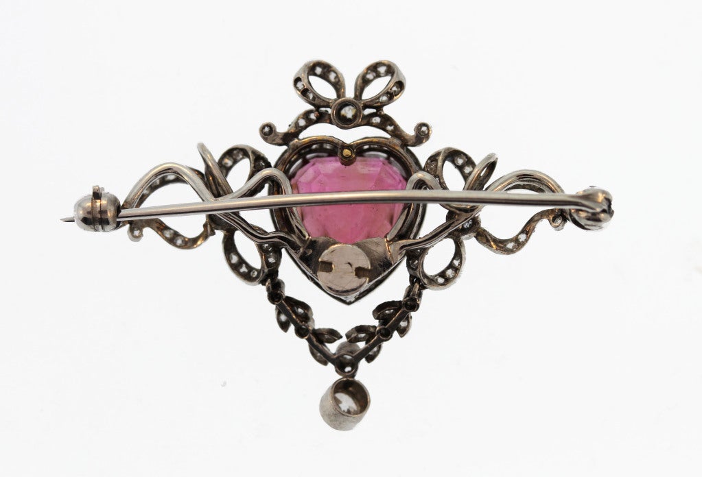 This sweet brooch features a heart-shaped pink tourmaline framed by garland and bows set with rose-cut and old European-cut diamonds.  A stylish one-of-a-kind jewel that can be worn as a brooch or pendant.