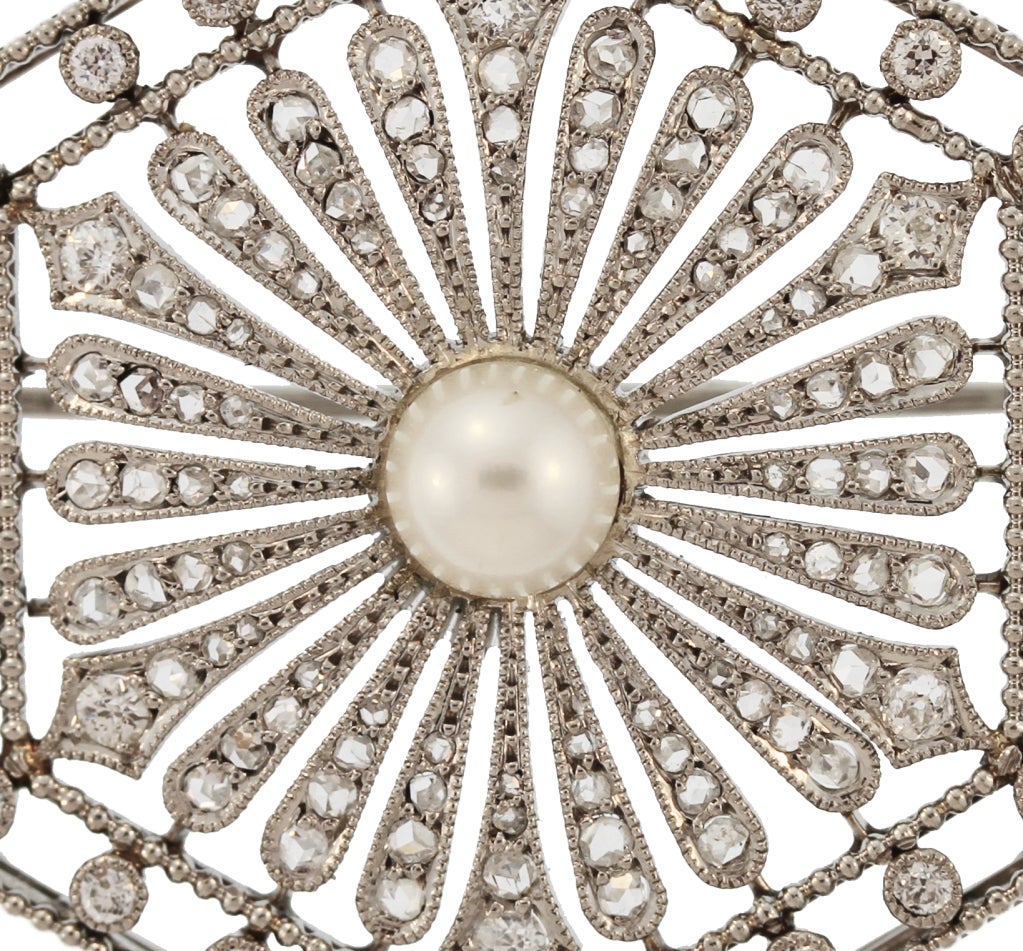 This delicate pin in set in the center with a pearl framed by graduated platinum band of milgrain work all within an openwork frame, set throughout with rose-cut diamonds.  Fitted at the back with a pendant hook this pin can either be worn as a