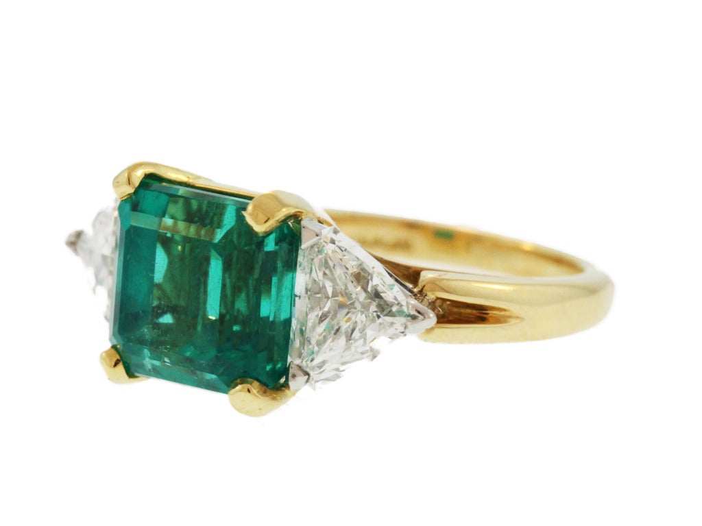 This beautiful ring, made by the American jewelry firm Oscar Heyman & Brothers, is set in the center with an emerald-cut emerald weighing 6.46 carats, flanked by 2 shield-shaped diamonds weighing approximately 1.90 carats, size 7 1/2, gross weight