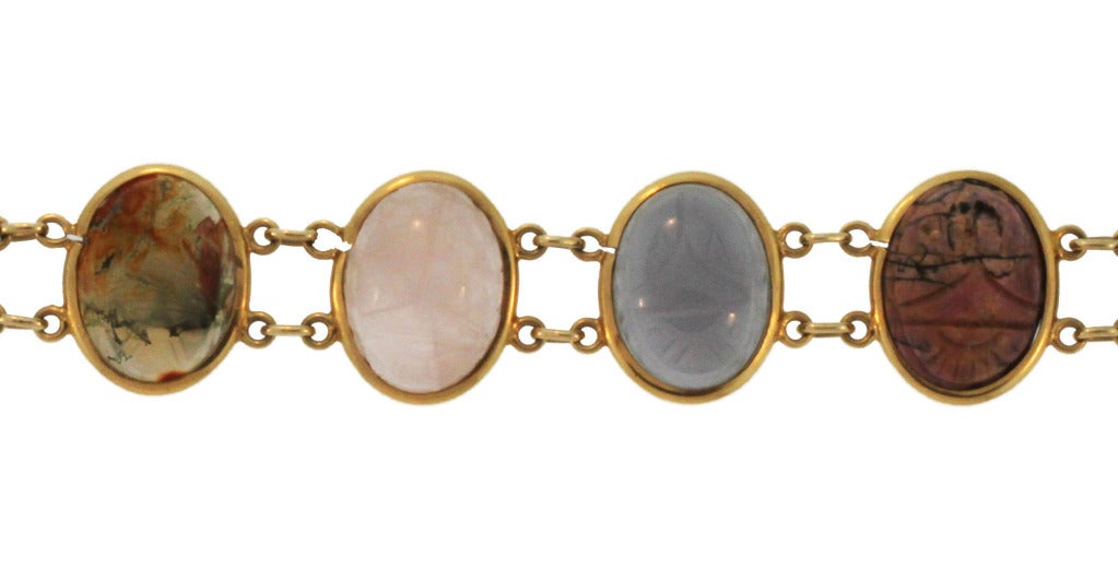 This unique bracelet is composed of 8 various carved hardstone scarabs collet-set and connected by links, mounted in 14 karat yellow gold.  In the style of egyptian-revival, this bracelet features the scarab image which was a revered symbol during