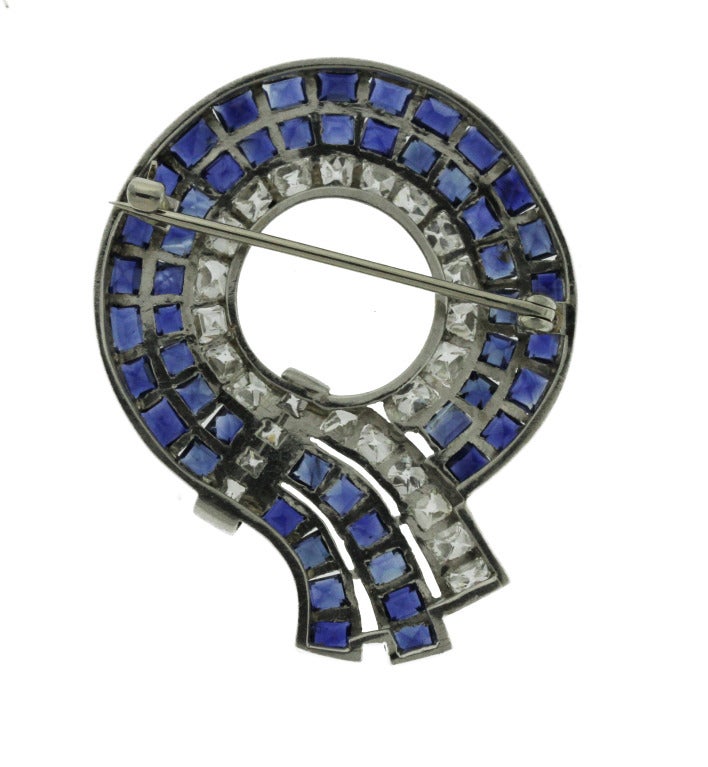 Designed as a circular bow set with 51 emerald-cut sapphires of a very vibrant deep blue hue weighing approximately 11.00 carats, and 25 French-cut diamonds weighing approximately 4.25 carats, gross weight 13.5 grams, measuring 1 3/4 by 1 3/8 by 1/8