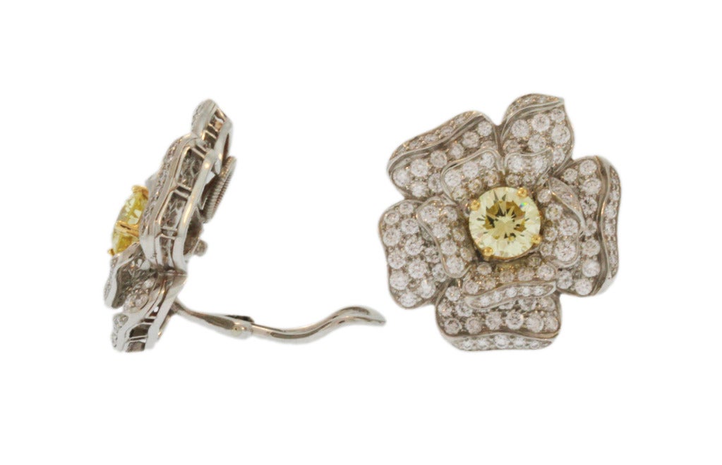 A Pair of Platinum Gardenia Earclips by Oscar Heyman & Brothers, designed as stylized gardenia flowers set in the centers with 2 round diamonds of fancy yellow color with GIA reports weighing 3.01 carats, the petals set with numerous round diamonds