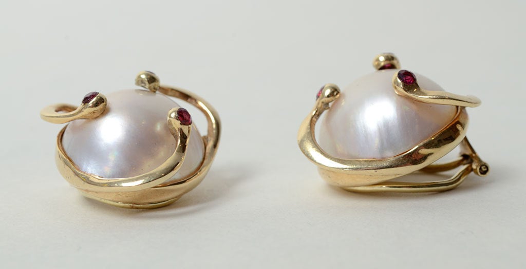 Unusual mabe pearl earrings with gold swirls tipped in rubies. The rubies add a touch of color to the large white pearls that measure 18.5 mm. The earrings have clip backs and are 1