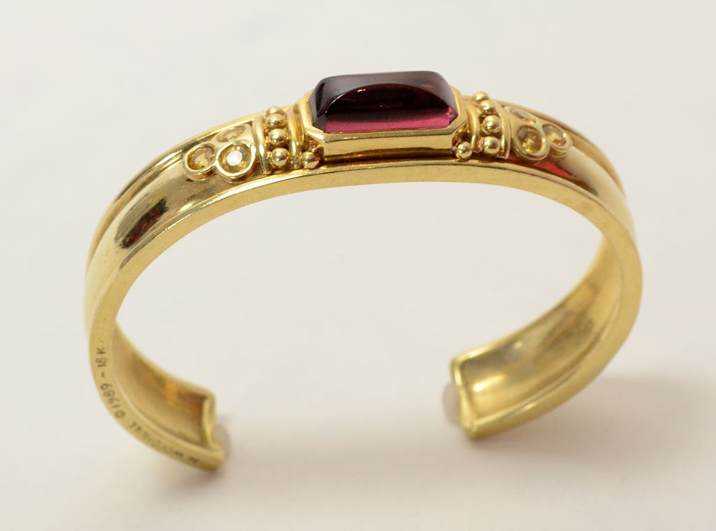 This is an original gold cuff bracelet by collectible American designer, Helen Woodhull. Since her death in 2005, Woodhull's atelier has continued at James Robinson but this piece is dated 1989.The central stone is garnet flanked by three yellow