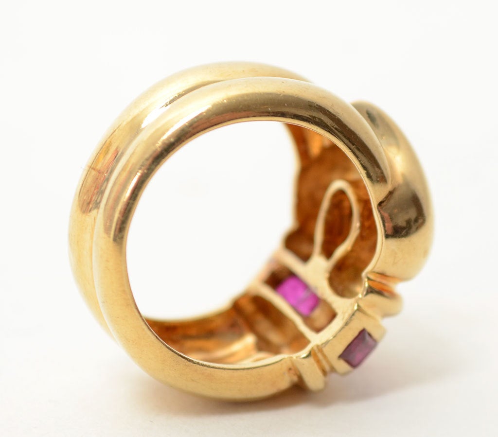 This is a wonderfully sculptural buckle ring in 18 karat gold with approximately 1 carat of rubies and a 12 point brilliant diamond. While actually made of one piece, the band looks as though it is comprised of two joined bands. Fits size 7.