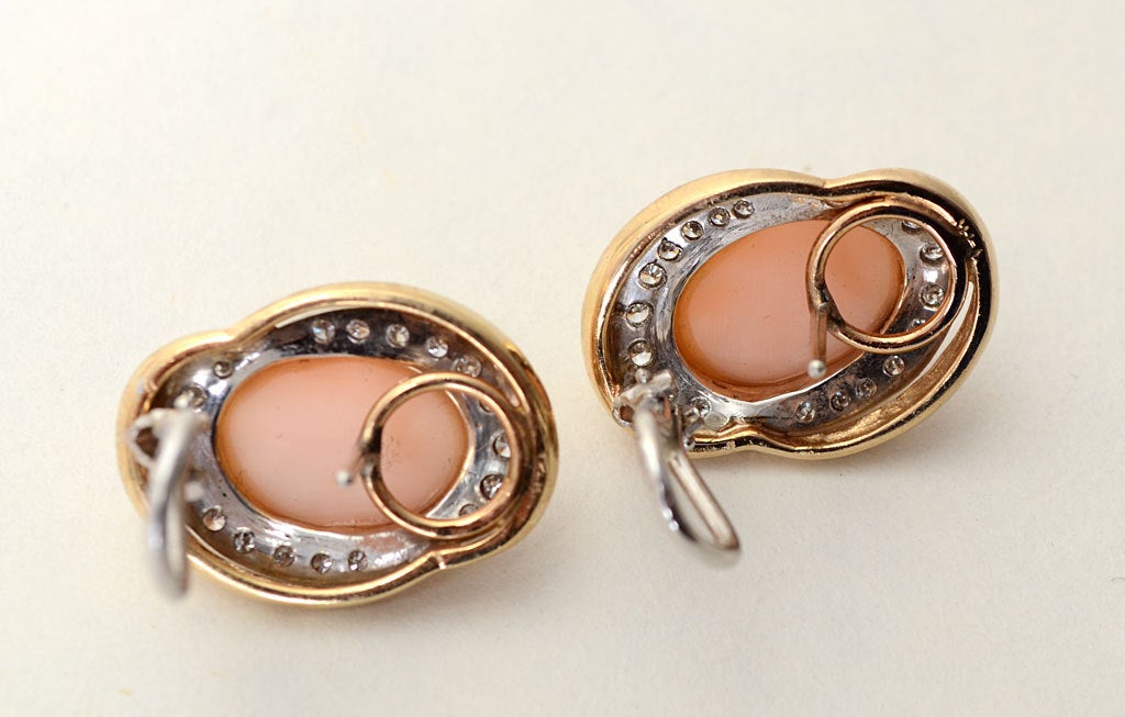 Refined and quietly elegant earrings in which a central coral stone is surrounded by diamonds. Set in 14 karat yellow gold with white gold backing. The earrings measure 3/4